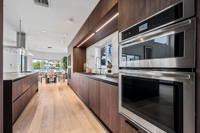 kitchen with dark brown cabinetry, sink, light wood-type flooring, and stainless steel double oven