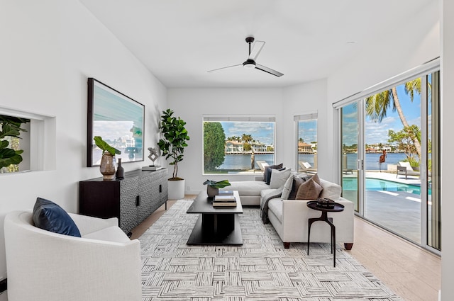 living room featuring ceiling fan, light wood-type flooring, a water view, and a wealth of natural light