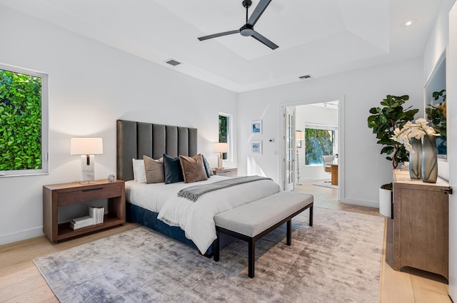 bedroom with connected bathroom, a tray ceiling, light hardwood / wood-style floors, and ceiling fan