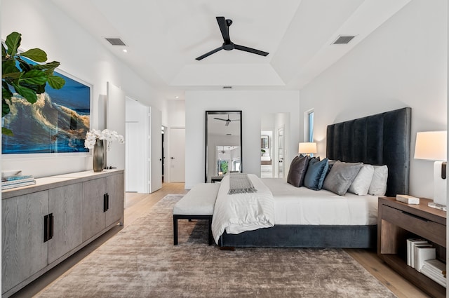 bedroom with ensuite bathroom, a tray ceiling, light hardwood / wood-style floors, and ceiling fan