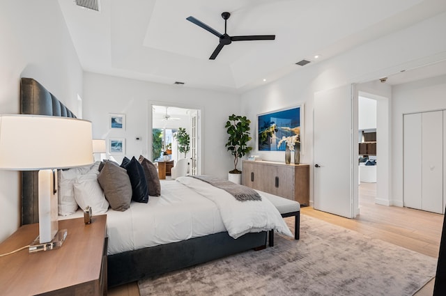 bedroom with ceiling fan, a raised ceiling, and light hardwood / wood-style floors