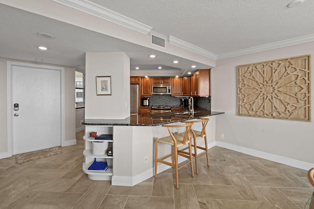 kitchen with a textured ceiling, stainless steel appliances, kitchen peninsula, and dark stone counters