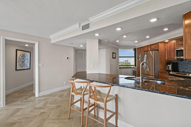 kitchen featuring a breakfast bar, dark stone countertops, kitchen peninsula, appliances with stainless steel finishes, and a textured ceiling