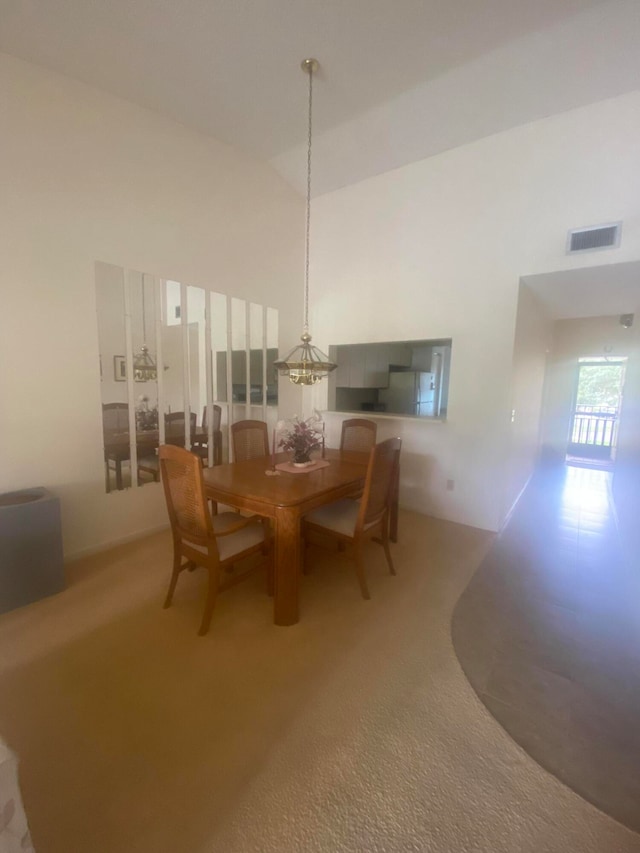 carpeted dining area with a notable chandelier and a high ceiling