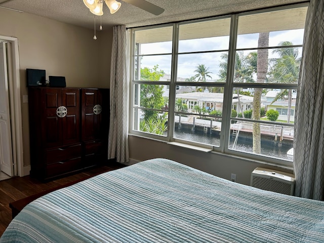 bedroom with multiple windows, a water view, dark hardwood / wood-style floors, and ceiling fan