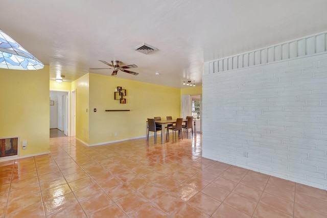 tiled spare room with ceiling fan and brick wall