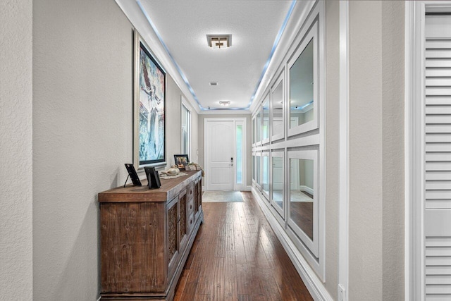 corridor with a textured wall, dark wood-type flooring, and visible vents