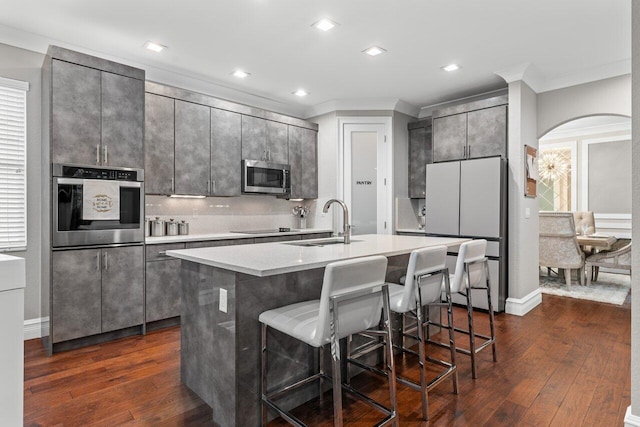 kitchen with arched walkways, an island with sink, a breakfast bar, stainless steel appliances, and a sink