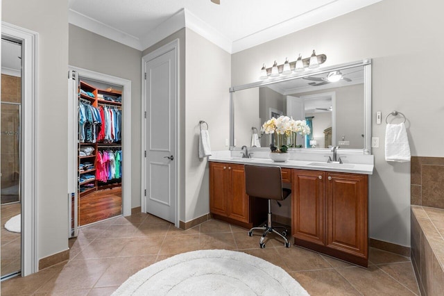 bathroom featuring a walk in closet, double vanity, ornamental molding, a sink, and tile patterned floors