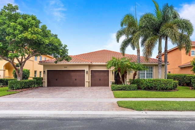 mediterranean / spanish house with a tiled roof, an attached garage, decorative driveway, a front lawn, and stucco siding