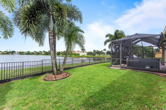 view of yard with a lanai, a water view, and fence