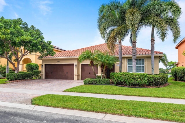 mediterranean / spanish house featuring stucco siding, a tiled roof, an attached garage, decorative driveway, and a front yard