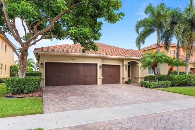 mediterranean / spanish home featuring a garage, a tiled roof, decorative driveway, and stucco siding