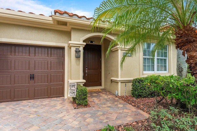 entrance to property featuring a tile roof, an attached garage, and stucco siding