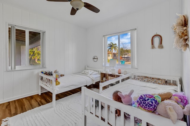 bedroom featuring ceiling fan, wood walls, and wood-type flooring