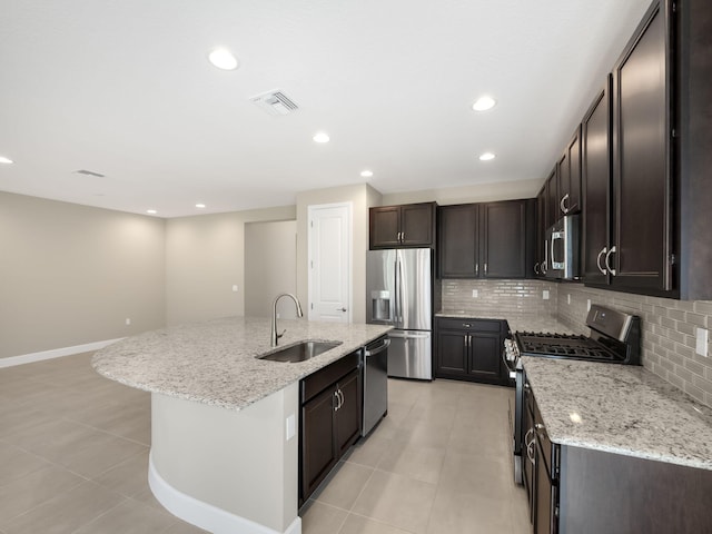 kitchen with decorative backsplash, a kitchen island with sink, light tile patterned floors, appliances with stainless steel finishes, and light stone counters