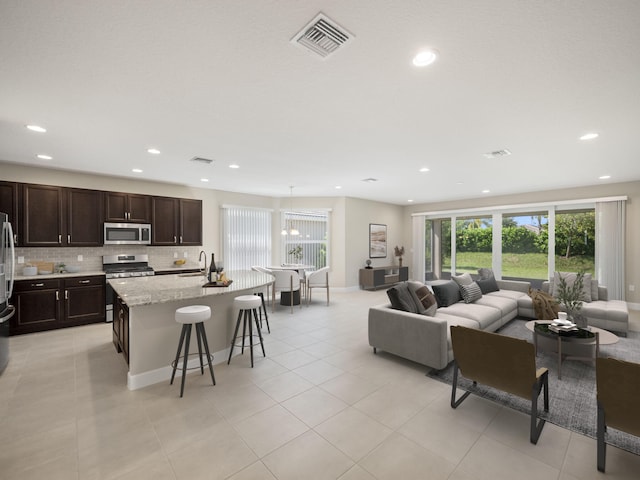 kitchen featuring tasteful backsplash, light stone countertops, appliances with stainless steel finishes, an island with sink, and a kitchen breakfast bar