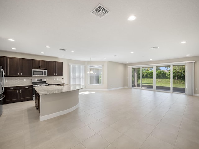 kitchen featuring stainless steel appliances, light stone counters, decorative backsplash, light tile patterned floors, and a center island with sink