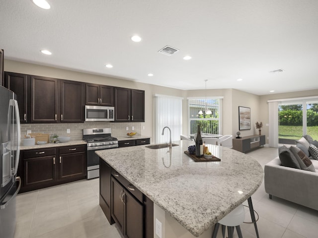 kitchen featuring sink, appliances with stainless steel finishes, decorative backsplash, and an island with sink