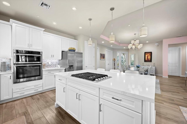 kitchen with decorative backsplash, light hardwood / wood-style flooring, stainless steel appliances, decorative light fixtures, and white cabinetry