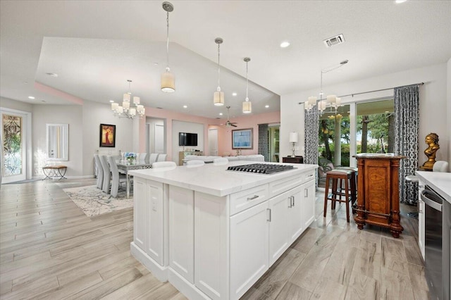 kitchen featuring hanging light fixtures, a kitchen island, white cabinetry, light wood-type flooring, and stainless steel gas cooktop