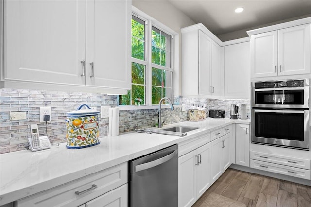 kitchen featuring decorative backsplash, appliances with stainless steel finishes, white cabinetry, light hardwood / wood-style flooring, and sink