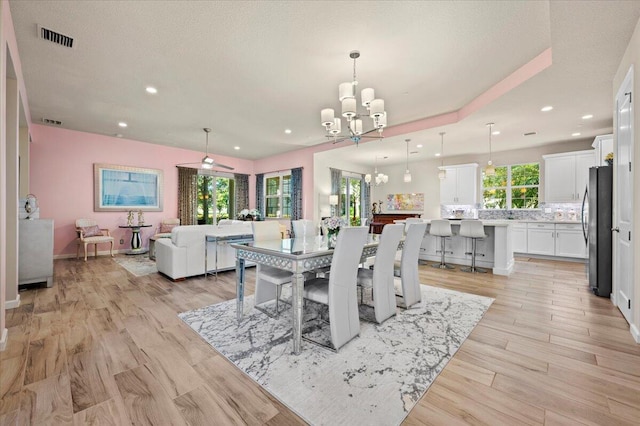 dining area featuring light hardwood / wood-style floors, a wealth of natural light, and ceiling fan with notable chandelier