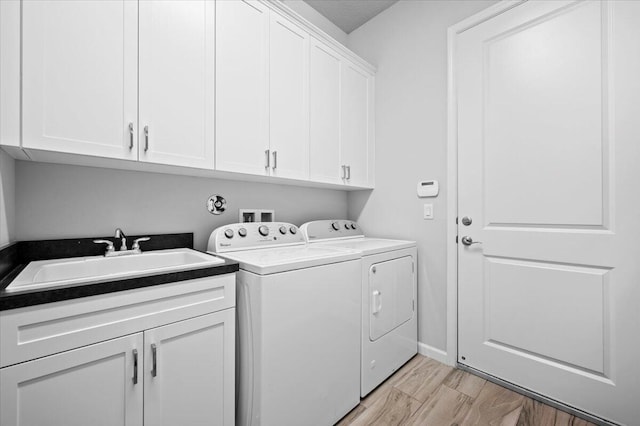 laundry area with sink, light hardwood / wood-style flooring, washer and dryer, and cabinets