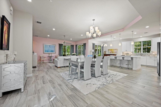 dining space with light hardwood / wood-style flooring, ceiling fan with notable chandelier, and plenty of natural light