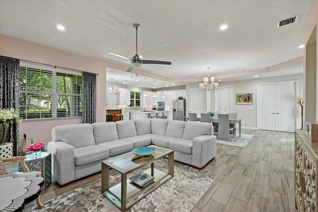 living room with a textured ceiling, ceiling fan with notable chandelier, light hardwood / wood-style floors, and a raised ceiling