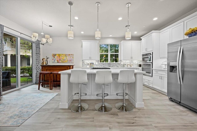 kitchen with a wealth of natural light, appliances with stainless steel finishes, decorative light fixtures, and white cabinets