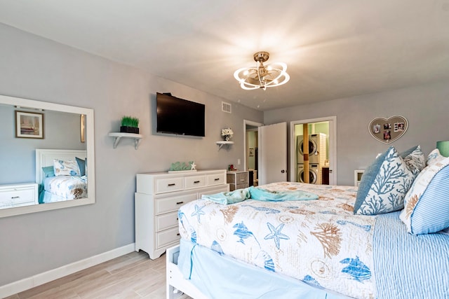 bedroom with stacked washer and dryer, a notable chandelier, and light hardwood / wood-style floors