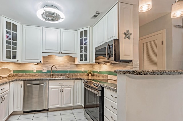 kitchen with stainless steel appliances, dark stone countertops, tasteful backsplash, and white cabinetry