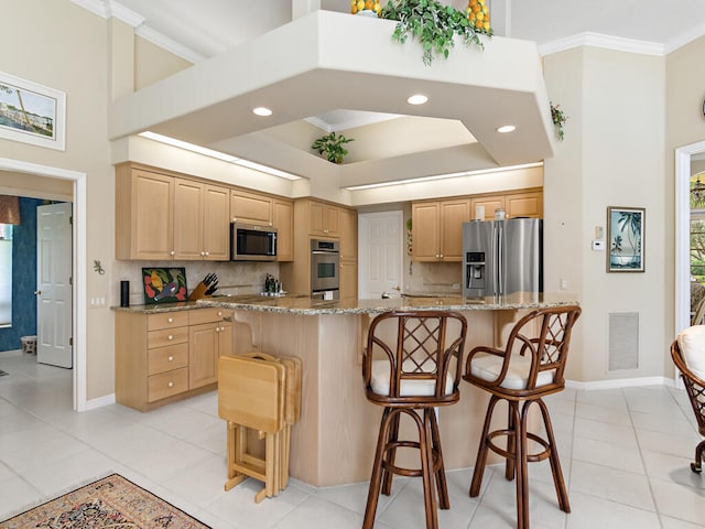 kitchen featuring a kitchen island, light stone counters, light brown cabinets, a breakfast bar area, and appliances with stainless steel finishes