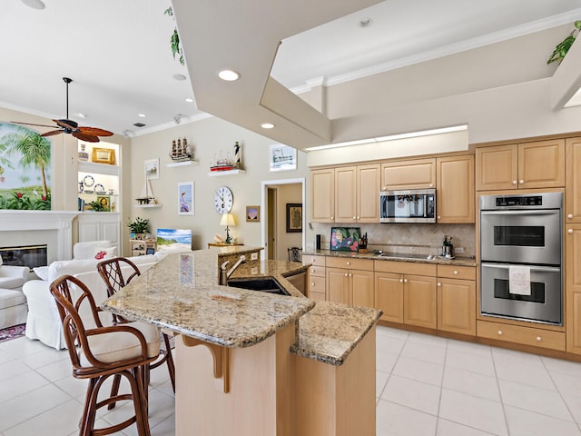 kitchen featuring light brown cabinetry, a breakfast bar area, a center island with sink, light stone counters, and appliances with stainless steel finishes