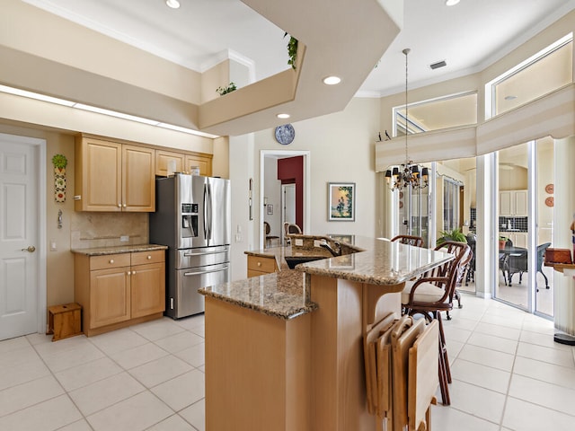 kitchen with an inviting chandelier, light stone counters, an island with sink, stainless steel refrigerator with ice dispenser, and ornamental molding