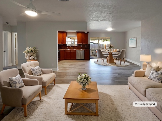 living room with a textured ceiling, sink, light wood-type flooring, and ceiling fan