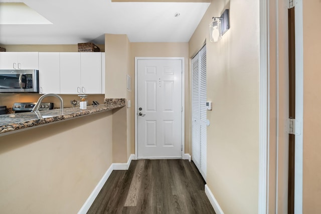 kitchen with stainless steel appliances, dark wood-type flooring, dark stone counters, and white cabinetry