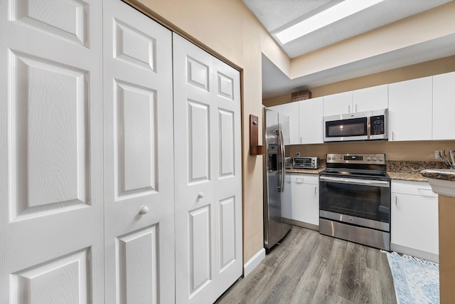 kitchen with white cabinets, stainless steel appliances, and light wood-type flooring