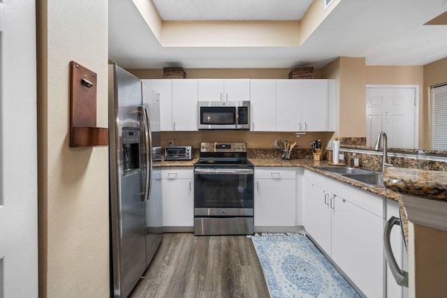 kitchen with dark stone countertops, stainless steel appliances, hardwood / wood-style floors, and white cabinetry