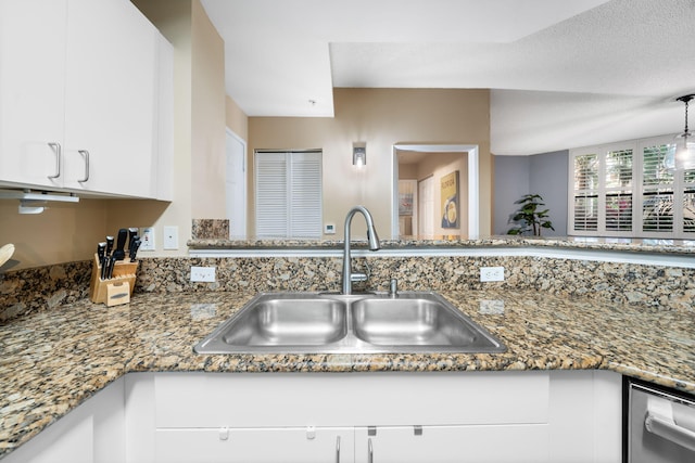 kitchen with stainless steel dishwasher, white cabinets, dark stone countertops, sink, and a textured ceiling