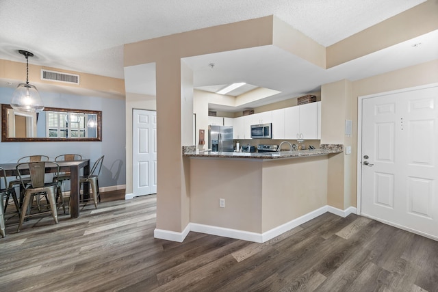 kitchen with stainless steel appliances, kitchen peninsula, white cabinets, and dark hardwood / wood-style flooring