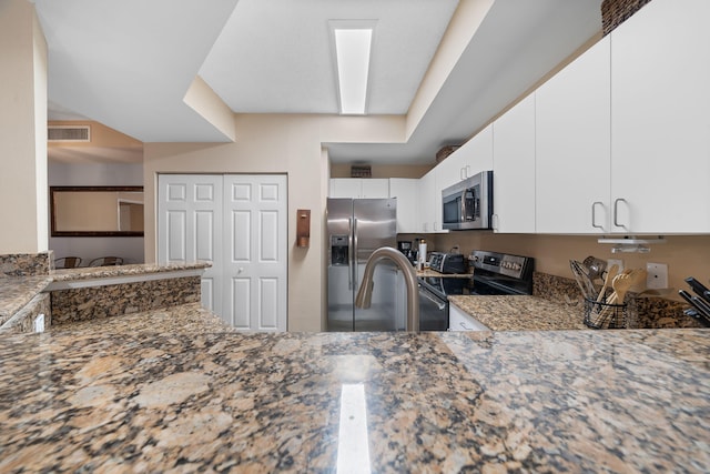 kitchen featuring sink, kitchen peninsula, white cabinetry, appliances with stainless steel finishes, and dark stone counters