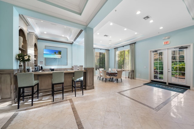 interior space featuring crown molding, a breakfast bar, a raised ceiling, kitchen peninsula, and french doors