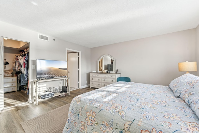 bedroom with a spacious closet, a closet, a textured ceiling, and dark hardwood / wood-style floors