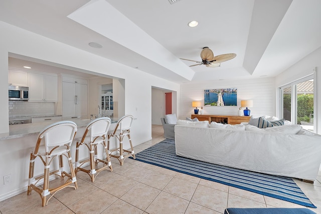 tiled living room with a raised ceiling and ceiling fan