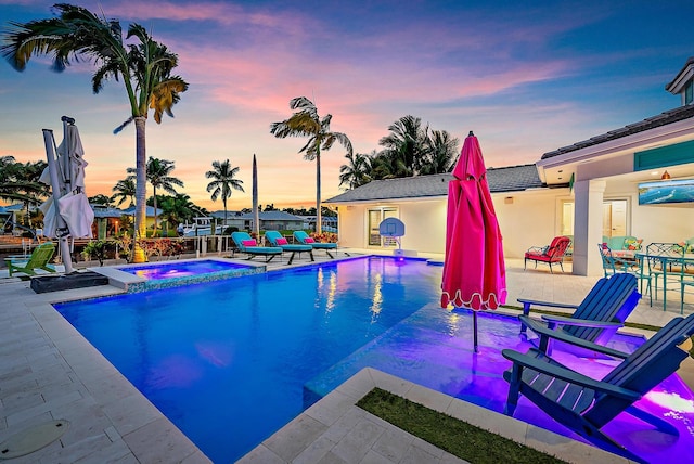 pool at dusk featuring an in ground hot tub and a patio area