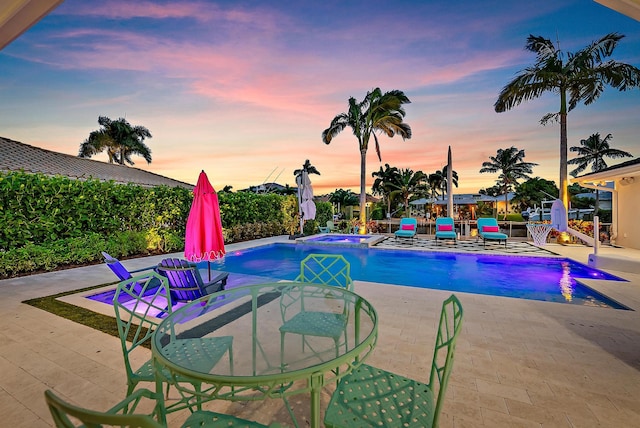 pool at dusk with an in ground hot tub and a patio area