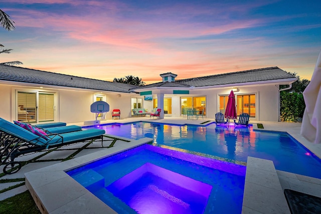 pool at dusk featuring a patio and an in ground hot tub