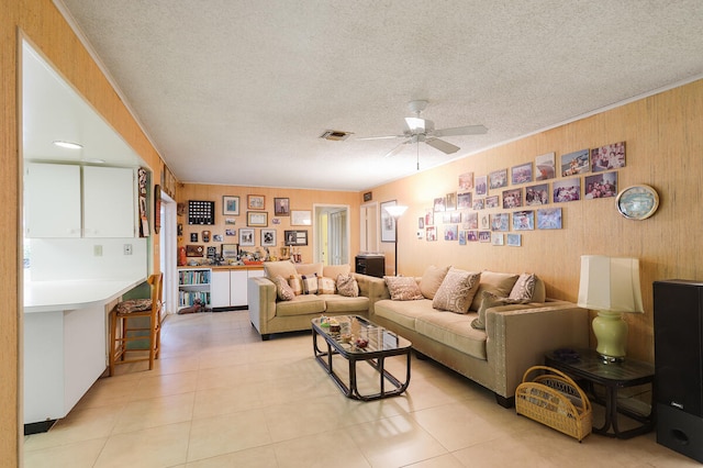 living room featuring wood walls, light tile patterned flooring, a textured ceiling, and ceiling fan